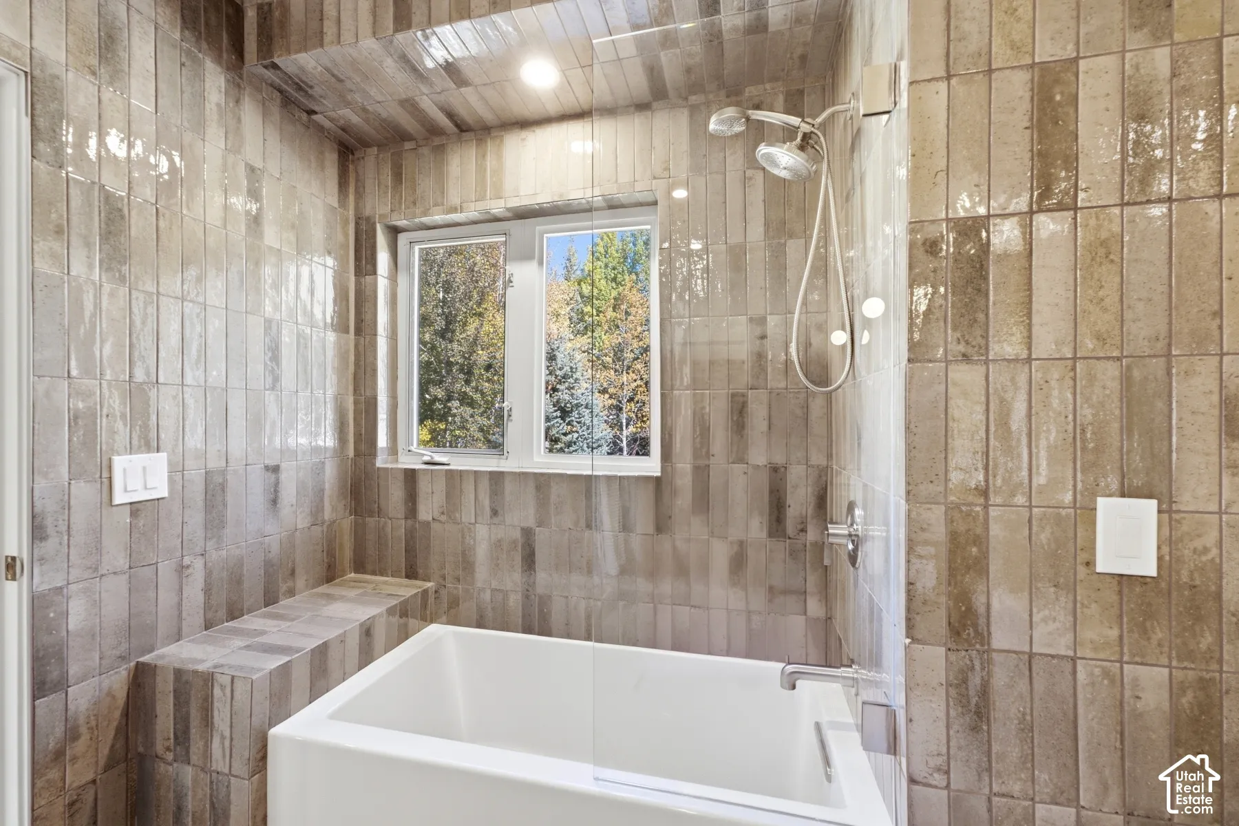 Subway tile surround, built-in tiled bench, white soaking tub, window with natural light, and a chrome shower head with a handheld sprayer