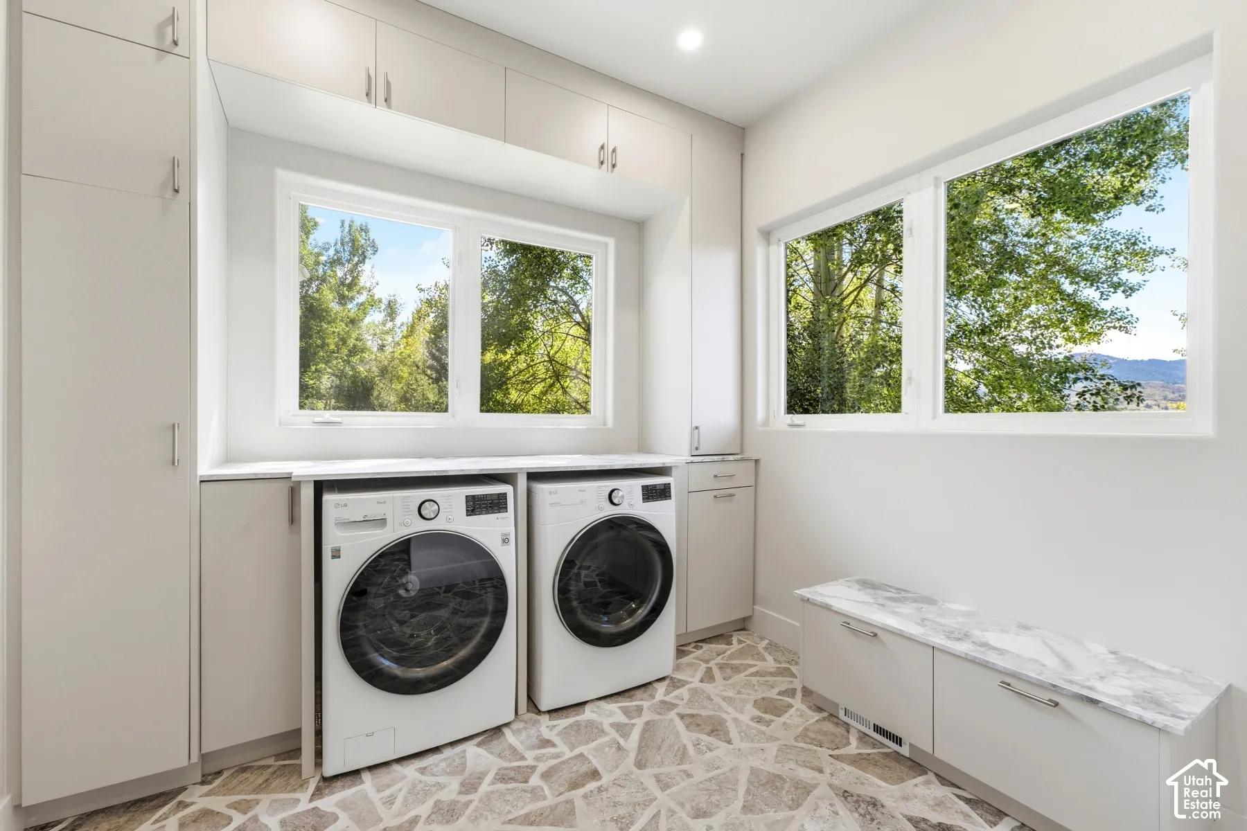 Laundry area with built-in cabinetry, stone-finish flooring, two large windows, and a countertop with integrated sink
