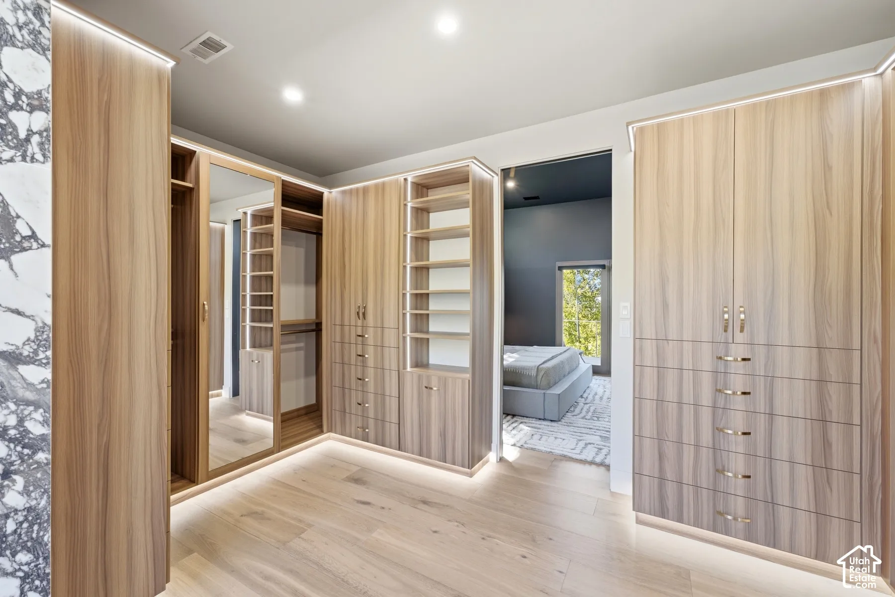 Custom built-in closet system with integrated lighting, wood-finish cabinetry, and a full-length mirrored door