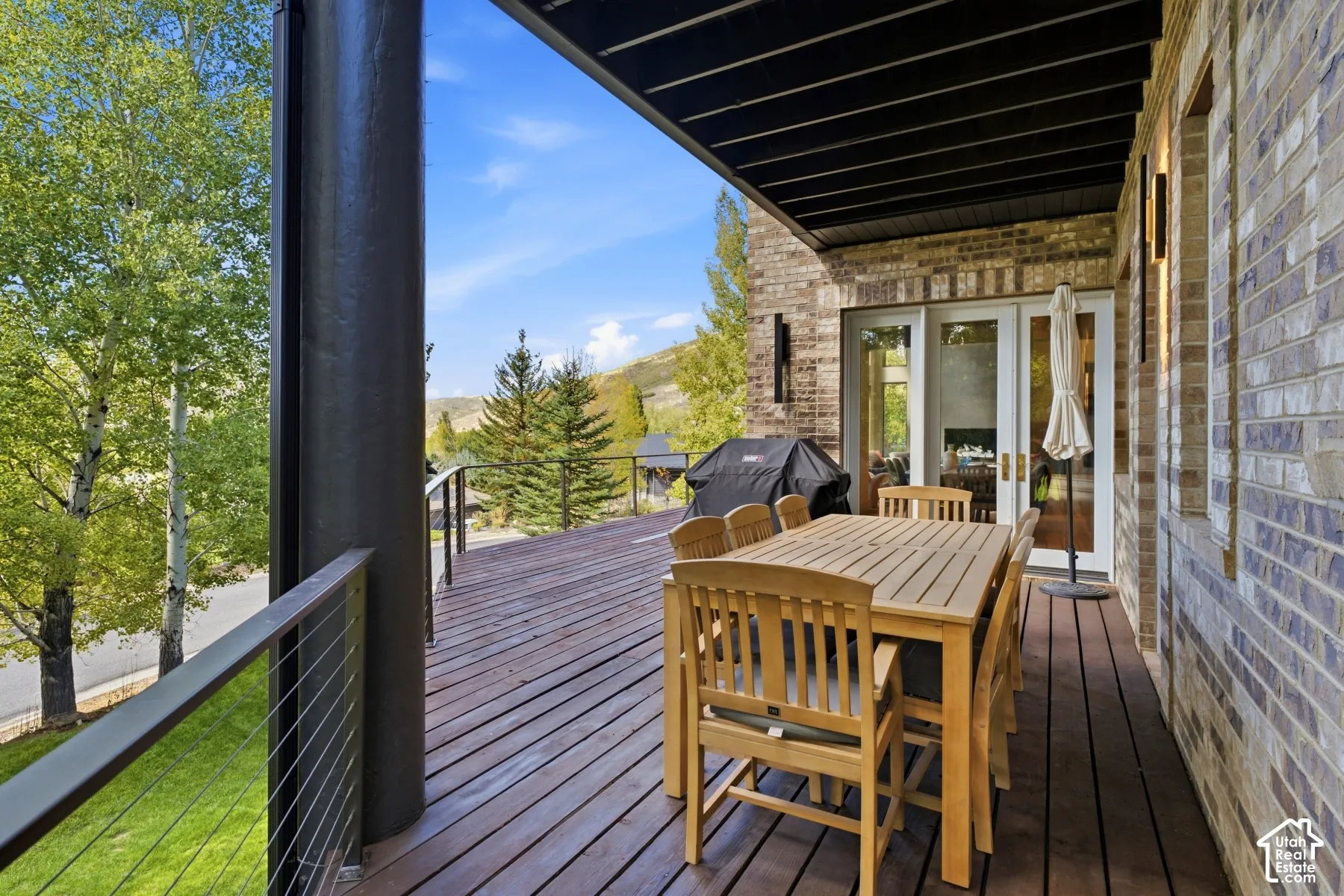 Expansive outdoor deck with wood-finish flooring, cable railing, brick exterior, and direct access through double doors