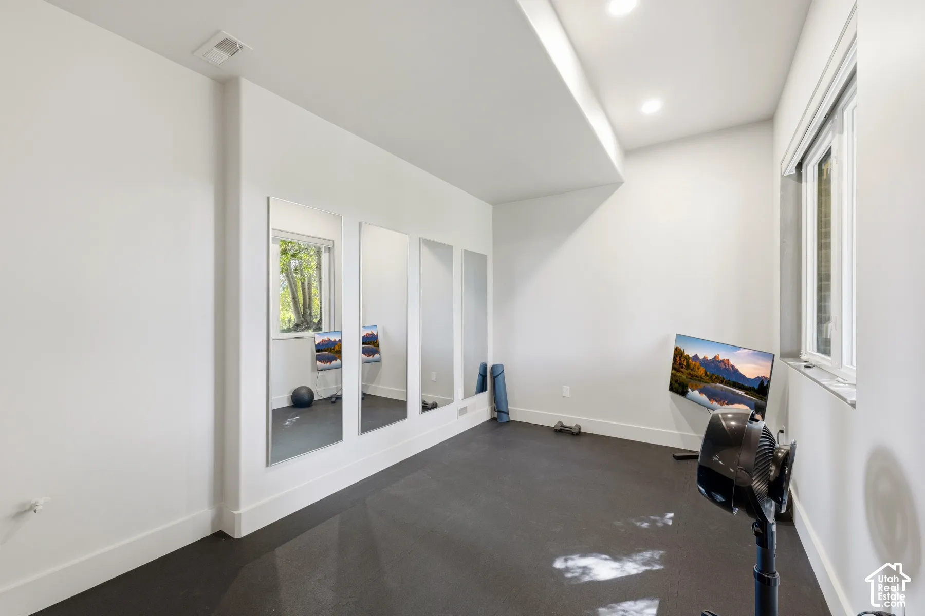 Room featuring dark-toned flooring, white walls, recessed ceiling lighting, and multiple wall-mounted mirrors