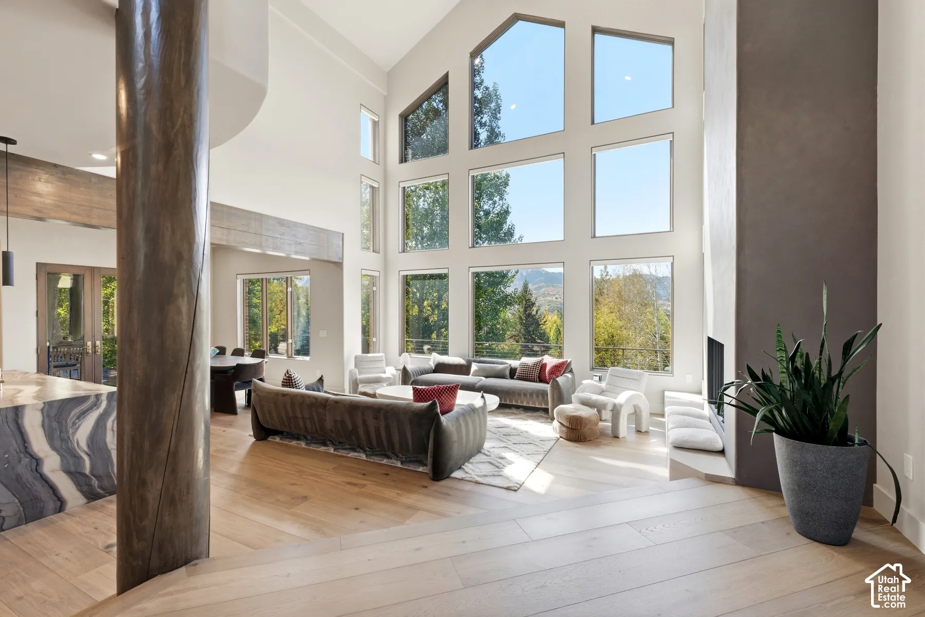 Vaulted ceiling with extensive window array, fireplace, light wood-finish flooring, and a stone-finish structural pillar