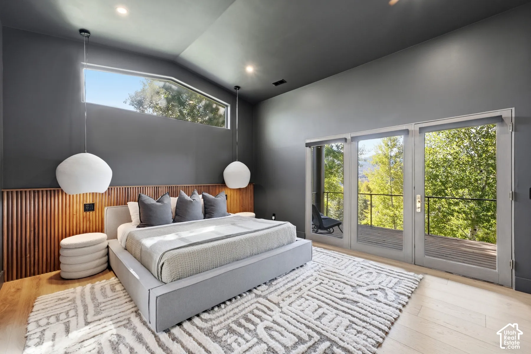 Vaulted ceiling with recessed lighting, wood-finish flooring, full-light French doors with balcony access, wood slat accent wall, and an elongated transom window