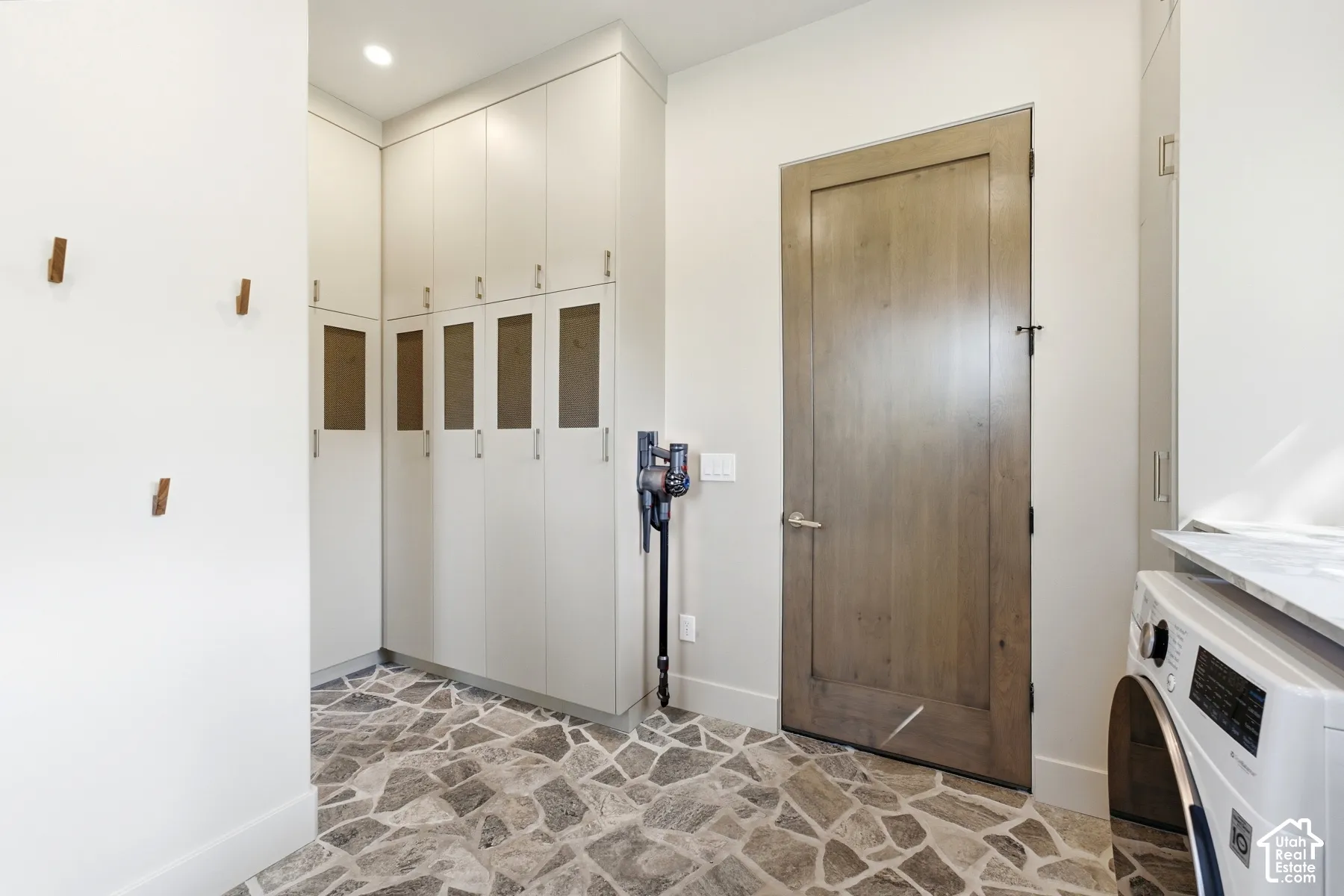 Built-in cabinetry with glass-fronted lower doors, wood-finish interior door, stone-finish flooring, and recessed ceiling lighting