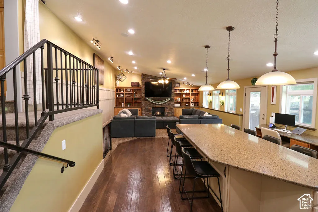 Vaulted ceiling with recessed lighting, wood-finish flooring, a stone-clad fireplace, and built-in shelving