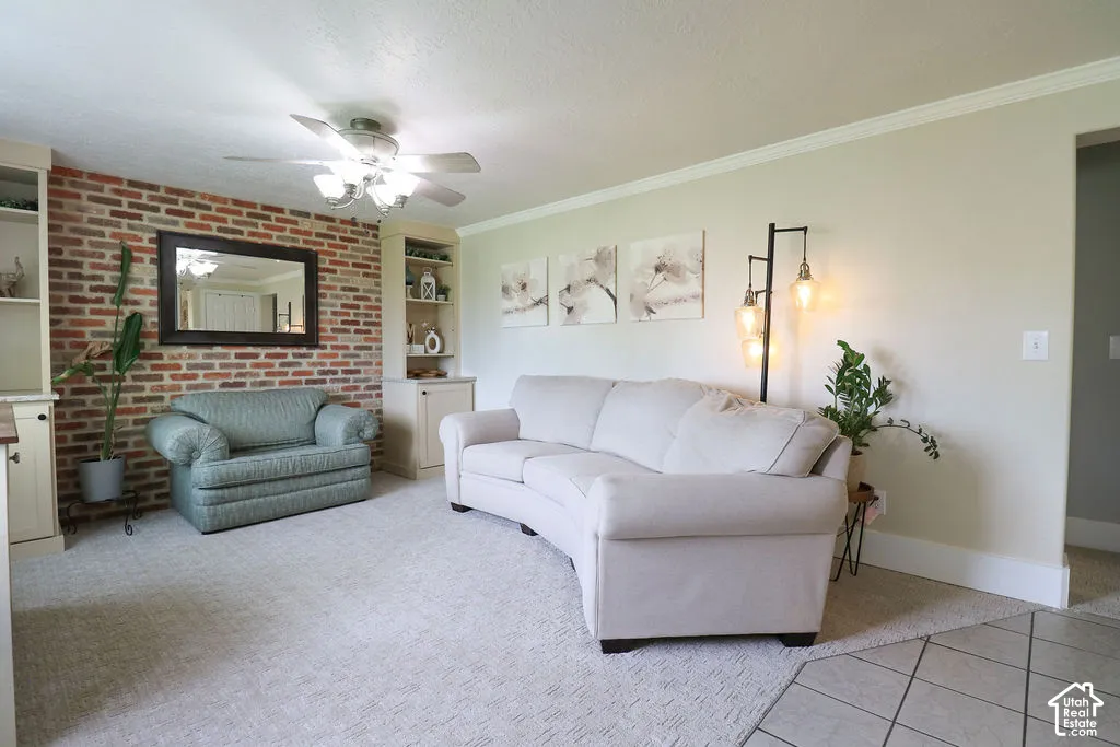 Exposed brick accent wall, built-in shelving, ceiling fan with light, crown molding, and neutral wall paint