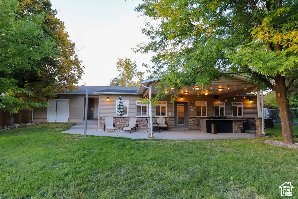 Expansive concrete patio with a covered outdoor entertaining area, featuring an integrated outdoor kitchen, multiple windows, and exterior lighting fixtures