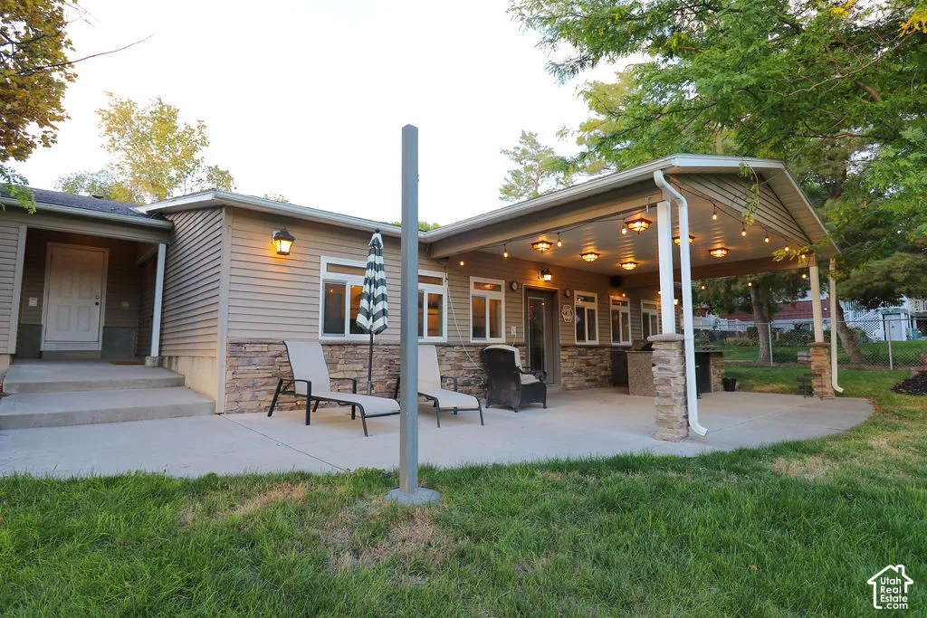 Exterior featuring horizontal siding, stone veneer accents, and a covered patio with string lighting