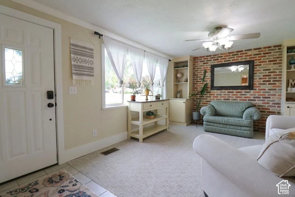 Entry area with tile flooring, leading to a carpeted living space with a brick accent wall and built-in shelving