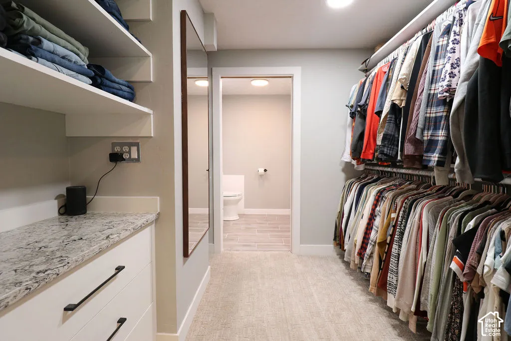 Walk-in closet featuring built-in shelving, white cabinetry with dark pulls, a stone-finish countertop, and full-length mirror