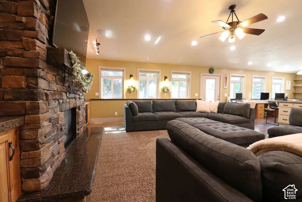 Stone-clad fireplace with a granite hearth, recessed lighting, ceiling fan, multiple windows, and built-in shelving