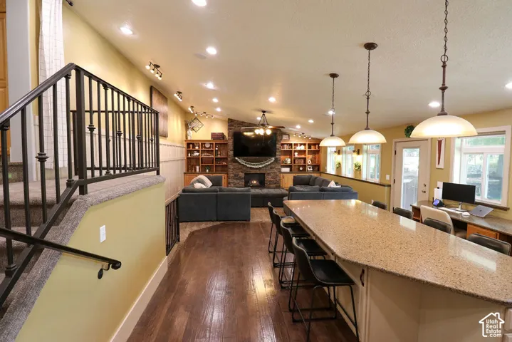 Vaulted ceiling with recessed lighting, wood-finish flooring, a stone-clad fireplace, and built-in shelving