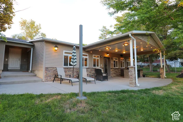 Exterior featuring horizontal siding, stone veneer accents, and a covered patio with string lighting