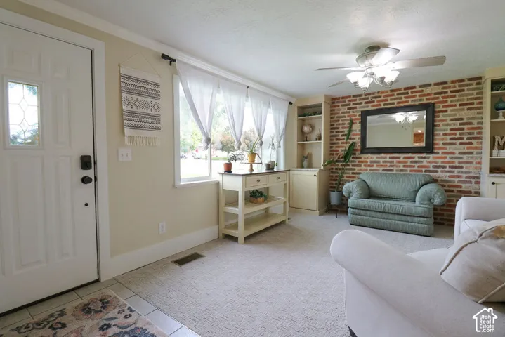 Entry area with tile flooring, leading to a carpeted living space with a brick accent wall and built-in shelving