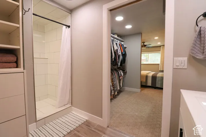 Walk-in shower with white tile surround, built-in shelving, wood-finish flooring, and recessed lighting