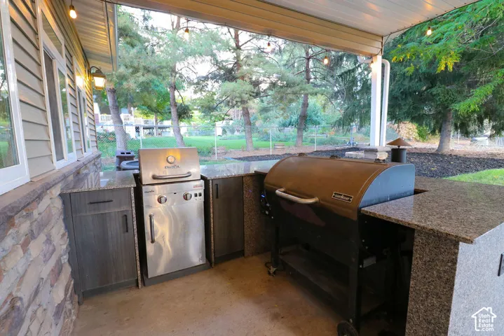 Covered patio featuring an outdoor kitchen with granite countertops, built-in cabinetry, and integrated grill