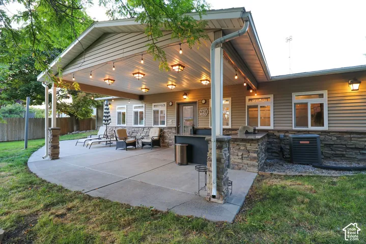 Expansive concrete patio with an extensive covered area, integrated outdoor kitchen with stone-clad base, and multiple overhead light fixtures