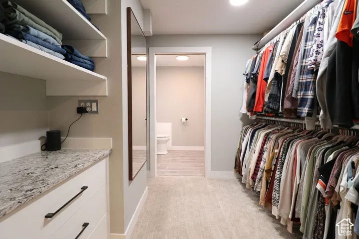 Walk-in closet featuring built-in shelving, white cabinetry with dark pulls, a stone-finish countertop, and full-length mirror