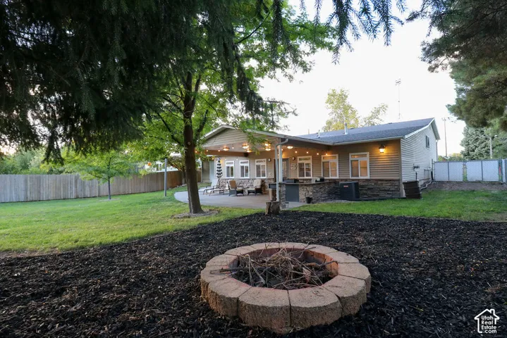 Expansive backyard featuring a manicured lawn, established trees, and a stone-paver fire pit