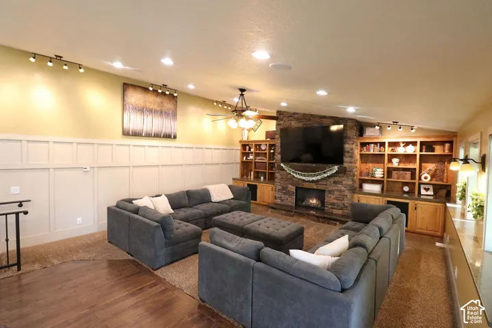 Stone-clad fireplace with a hearth, integrated shelving and cabinetry, recessed ceiling lights, wood-finish flooring, and wainscoting