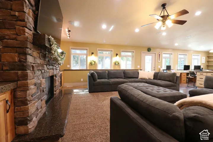 Stone-clad fireplace with a granite hearth, recessed lighting, ceiling fan, multiple windows, and built-in shelving
