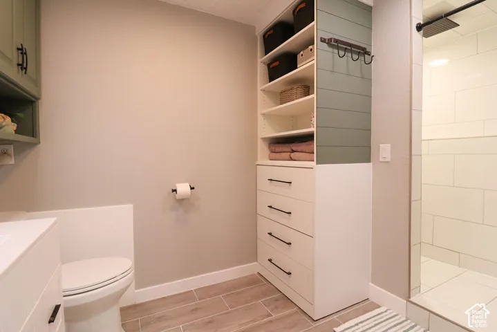 Wood-finish flooring, built-in storage with open shelving, four storage drawers, and a tiled shower with a dark-finish shower head