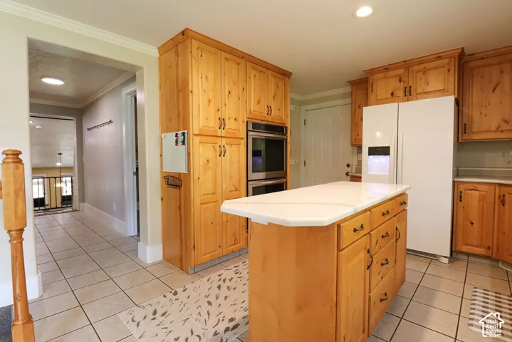 Spacious kitchen featuring warm wood cabinetry, a large central island with storage and countertop seating, stainless steel built-in appliances, white refrigerator, tile flooring, and recessed lighting throughout
