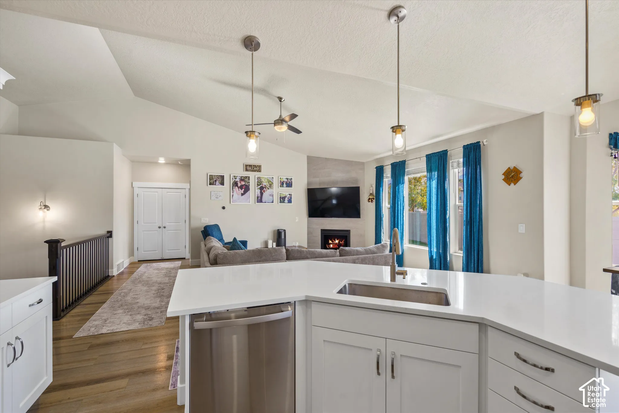 Vaulted ceilings with recessed lighting, kitchen island with integrated sink, stainless steel dishwasher, fireplace with stone surround, and wood-finish flooring