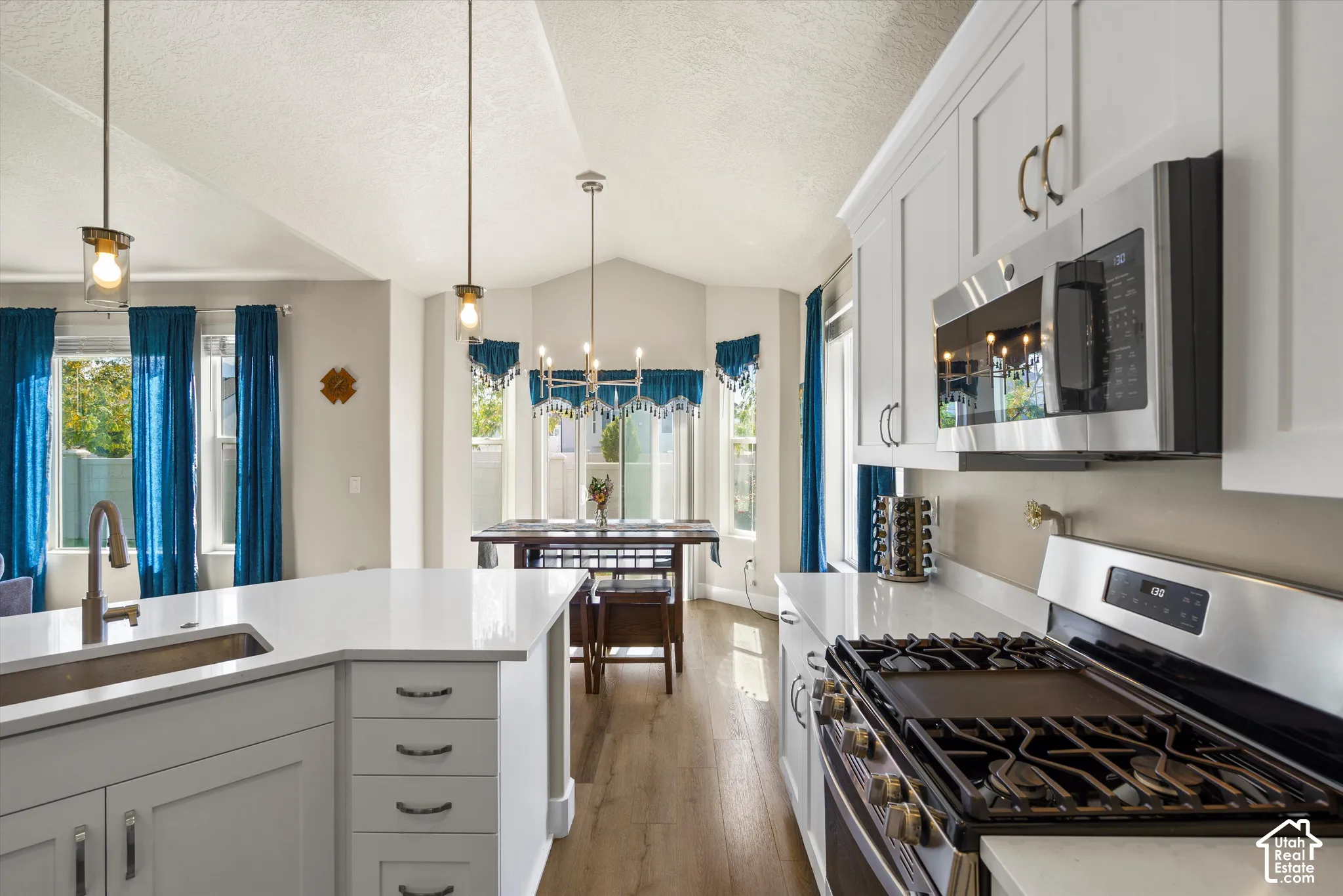 Spacious kitchen with white shaker cabinetry, stainless steel appliances, a center island with sink, and light-tone wood-finish flooring