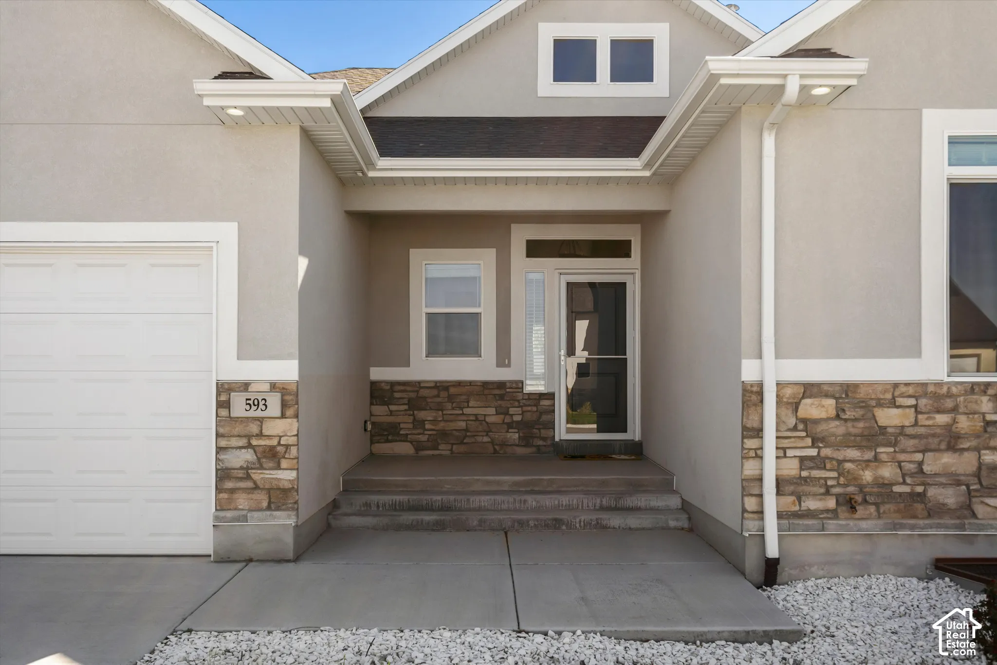 Stucco exterior with stone veneer accents, an attached garage, a covered entry, and a prominent front door