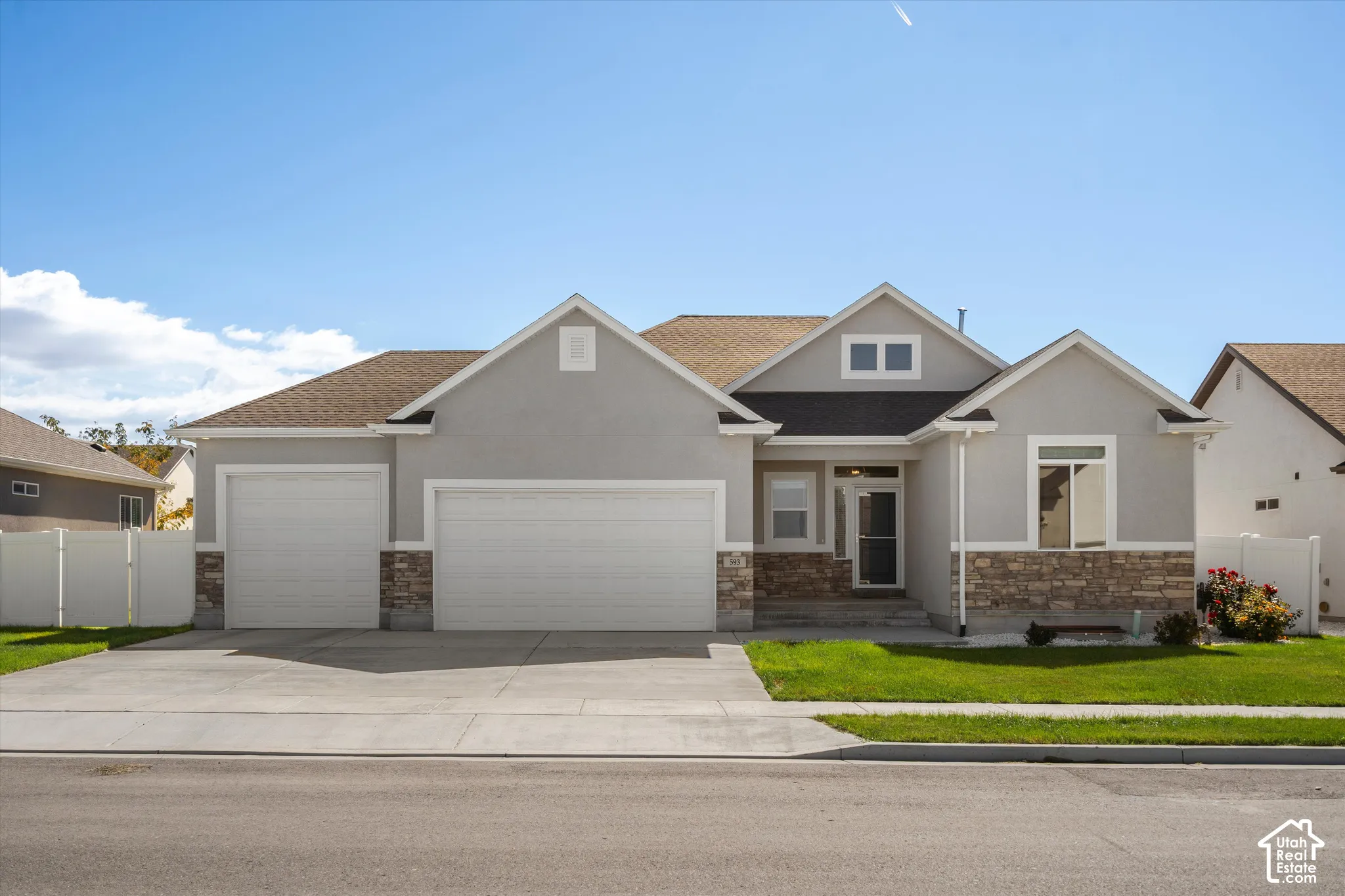 Gray stucco exterior with a stone accent facade, featuring a three-car garage and a paved driveway