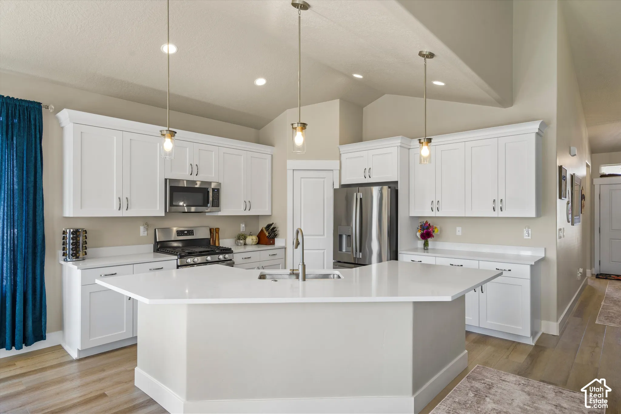 Kitchen featuring white shaker cabinetry, stainless steel appliances, a center island with sink, quartz countertops, and wood-finish flooring