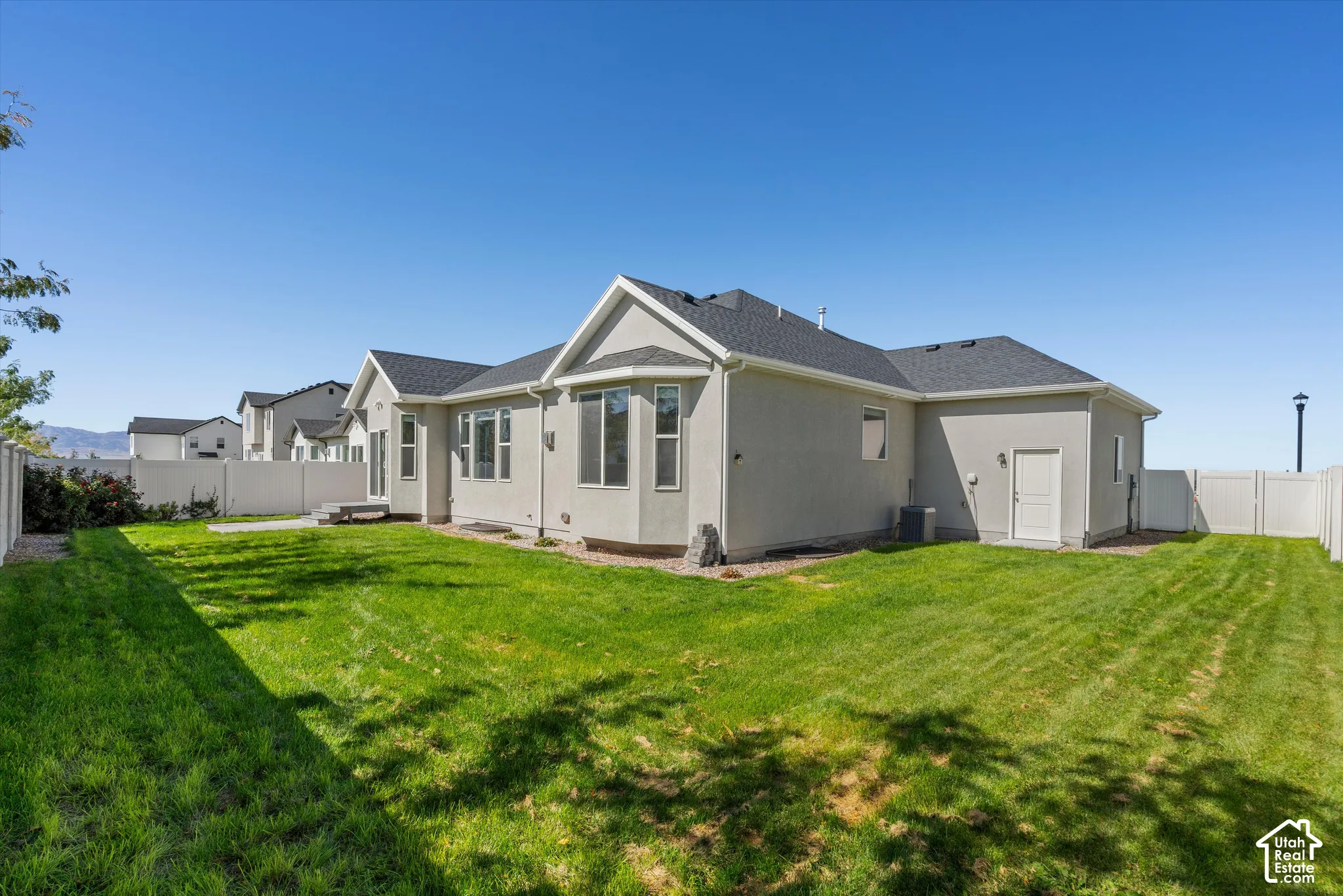 Expansive backyard featuring a manicured lawn, stucco exterior, multiple windows, and privacy fencing