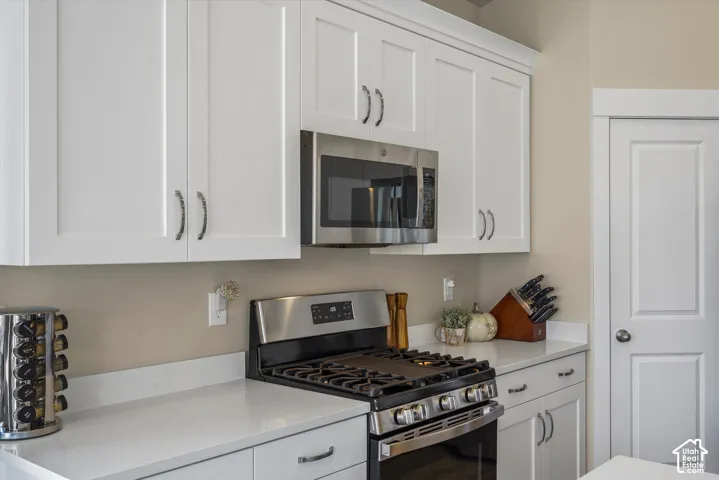 White shaker-style cabinetry, stainless steel microwave, stainless steel gas range, light-toned countertop, and a paneled door