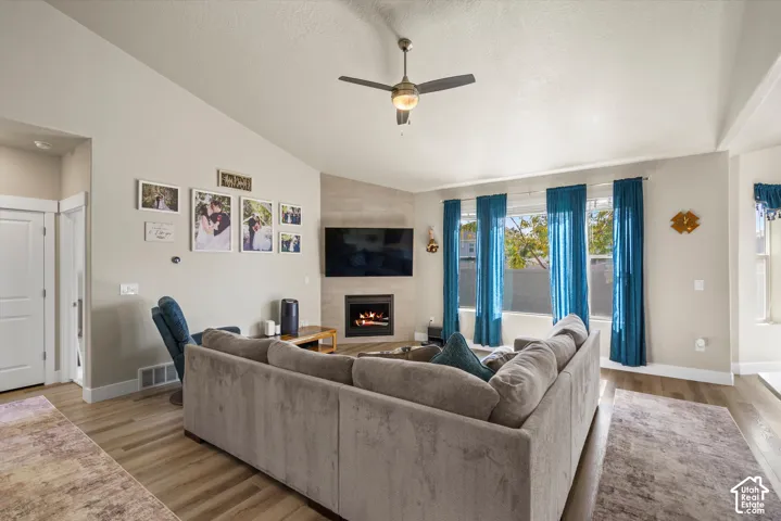 Vaulted ceiling with a ceiling fan, wood-finish flooring, built-in fireplace, and large windows