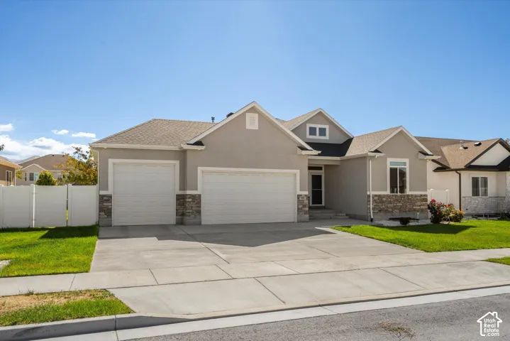 Stucco exterior with stone accents, three-car garage, concrete driveway, and front lawn