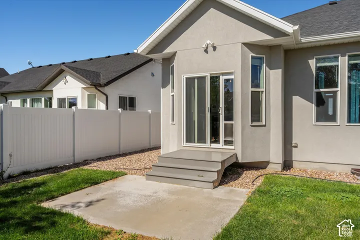 Sliding glass door access to the exterior, concrete patio, gravel landscaping, manicured lawn, and privacy fencing