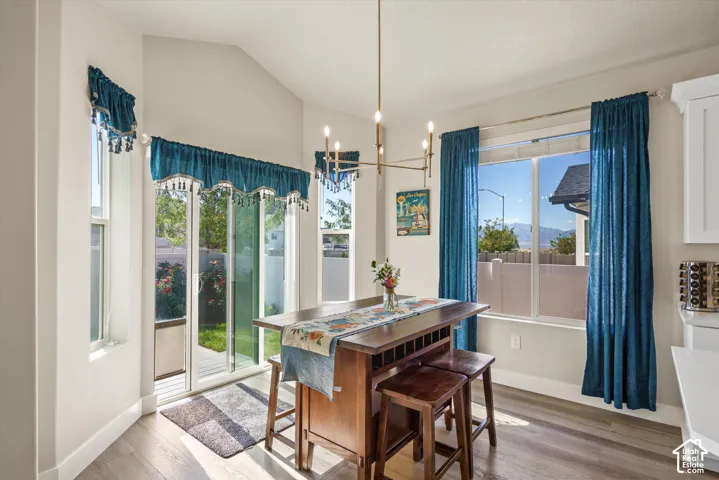 Vaulted ceiling with a chandelier, wood-finish flooring, and white cabinetry