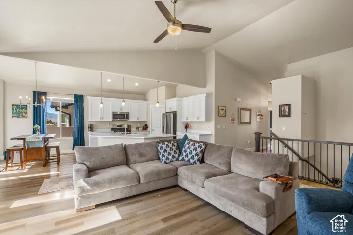 Vaulted ceilings with a ceiling fan, wood-finish flooring, white kitchen cabinetry, stainless steel appliances, and an island with pendant lighting