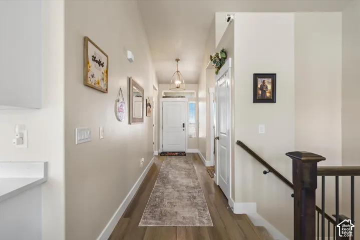 Wood-finish flooring, white trim, staircase with dark wood newel post and handrail, white interior doors, and a decorative pendant light fixture