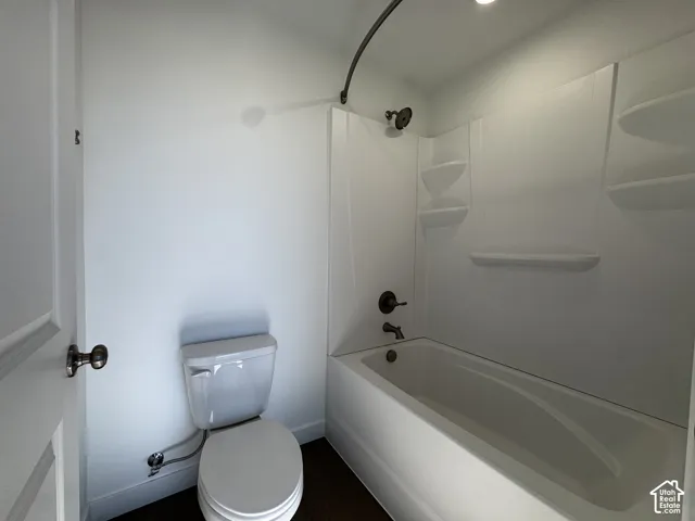 Bathroom featuring a white bathtub, integrated shower shelving, dark bronze fixtures, and wood-finish flooring