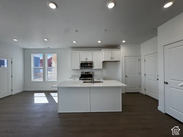 Contemporary kitchen featuring white cabinetry, a center island with a sink, stainless steel appliances, and dark wood-finish flooring