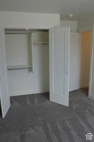 Plush gray carpet flooring, white painted walls, white trim, and a built-in closet with shelving and hanging rods
