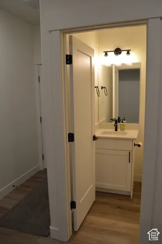 Powder room featuring a single vanity with a white countertop, wood-finish flooring, and a wall-mounted light fixture