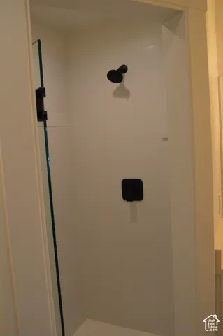 Walk-in shower featuring a glass enclosure, white paneling, and matte black fixtures