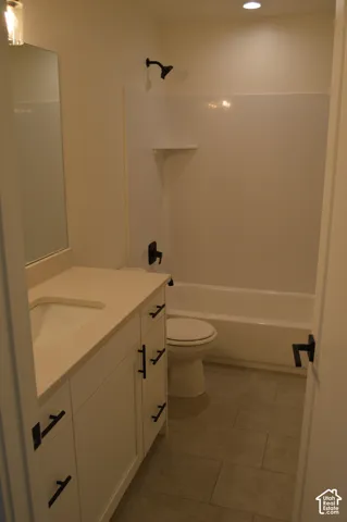Vanity with integrated sink and stone-finish countertop, white cabinetry with matte black hardware, tiled flooring, and a white tub/shower combination with matte black fixtures