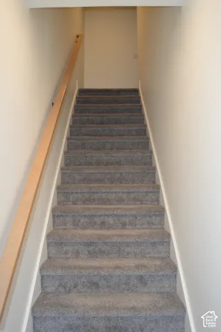 Staircase with gray carpeting and a light wood-finish handrail