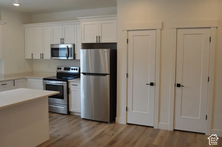 Kitchen featuring white cabinetry, stainless steel appliances, a center island, and wood-finish flooring