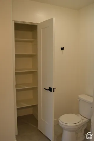 Built-in shelving, white paneled door, matte black door hardware, white toilet, and light-toned flooring