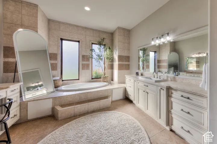 Built-in soaking tub, dual vanity with undermount sinks, extensive countertop space, wood-finish cabinetry, and tile flooring